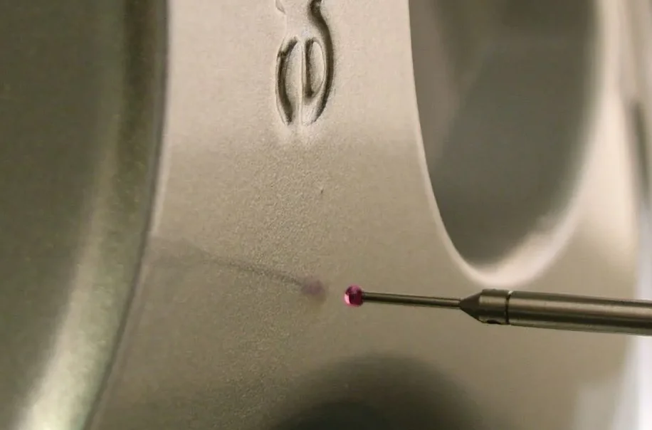 Pointe de stylo appliquée sur une surface métallique, avec une légère trace colorée.
Outil de métrologie.
